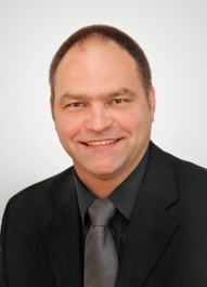 A person in a suit smiling Description automatically generated with low confidence